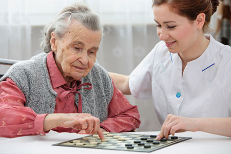 Senioren Tagespflege Pflegepersonal und Gast speilen ein Brettspiel